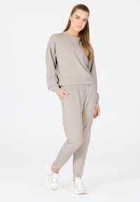 Ensemble sweat-shirt et pantalon gris clair fabriqué en tissu doux. Il présente des poignets et une taille côtelés, avec une coupe décontractée et des poches latérales.