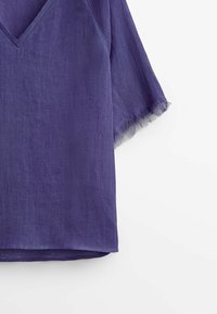 Haut violet en mélange de lin avec col en V, manches courtes et bords effilochés. Tissu léger et texturé avec une coupe décontractée.