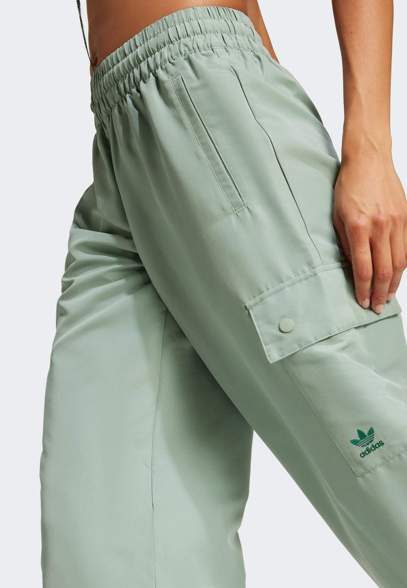 Pantaloni cargo verde chiaro con vita elasticizzata, tasche laterali e un piccolo logo adidas verde sulla gamba sinistra. Texture liscia.