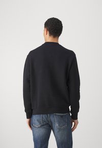 Musta pusero, jossa on pyöreä pääntie, resorit hihansuissa ja helmassa, sileällä pinnalla. Pusero yhdistetty sinisiin farkkuihin, joissa näkyy taskujen yksityiskohdat.