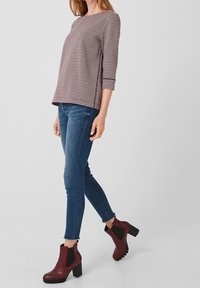 Top de patrón a cuadros con mangas tres cuartos, combinado con jeans skinny azules y botas de tobillo burdeos con tacón grueso y paneles laterales.