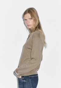 Brun stickad sweatshirt med långa ärmar och rund halsringning, kombinerad med mörk denimjeans. Har en avslappnad passform och minimalistisk design.