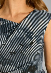 Wielokolorowa sukienka z dekoltem w szpic, ozdobiona ukośnymi paskami w kolorach niebieskim i czarnym oraz abstrakcyjnymi wzorami; gładka faktura tkaniny.