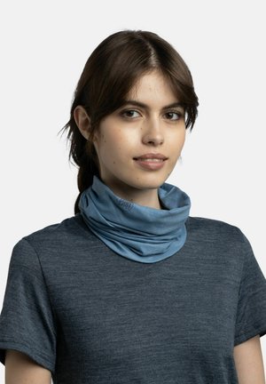 Junge Frau mit dunklen Haaren trägt einen blauen Schlauchschal und ein dunkelgraues Kurzarmshirt, schaut mit einem leichten Lächeln nach vorne.