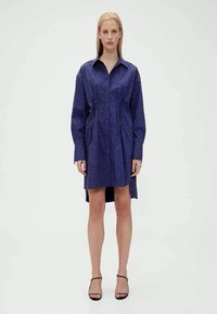 Vestido camisa azul-marinho com botões na frente, mangas compridas e cintura ajustada, apresentando um padrão delicado de pontos e comprimento até a metade da coxa.