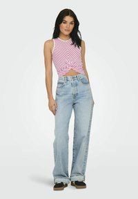 Top court rayé rose et blanc avec un devant noué, associé à un jean taille haute ample bleu clair et des baskets noires.