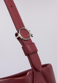 Bordowy pasek skórzany z okrągłymi, srebrnymi okuciami i zakładką do regulacji, z teksturowanym wykończeniem oraz miękkim, usztywnionym designem.