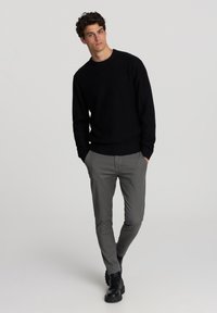 Maglione nero a maglia con texture a coste, scollo rotondo e maniche lunghe. Abbinato a pantaloni slim-fit grigi e stivali neri stringati.