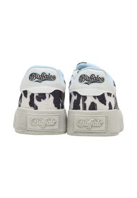 Paire de baskets de la marque Buffalo avec imprimé vache noir et blanc et semelles blanches, vue de dos.