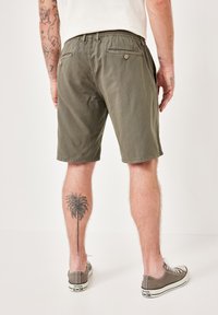 Olivgrüne Shorts mit einem elastischen Bund, ausgestattet mit Gesäßtaschen und einer glatten Textur. Getragen mit grauen Leinenschuhen.