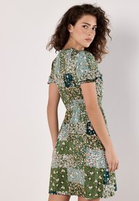 Bunt bedrucktes Kleid mit einem Patchwork-Design und floralen Mustern in Grüntönen und Blau, kurzen Ärmeln und tailliertem Schnitt.