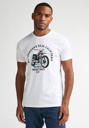 Witte katoenen t-shirt met een grafische print van een motorfiets en tekst. Korte mouwen, ronde hals en een losse pasvorm. Draagt blauw denim jeans.