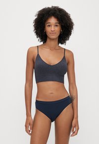 Granatowy biustonosz typu bralette z błyszczącą fakturą i regulowanymi ramiączkami, w połączeniu z dopasowanymi majtkami bikini w podobnym kolorze i wzorze.