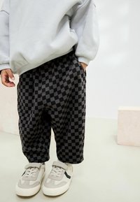 Schwarz-grau karierte Hose aus weichem Stoff, mit einem elastischen Bund und seitlichen Taschen, kombiniert mit hellen Sneakers.