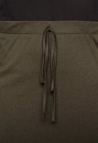 Close-up van olijfgroene stofbroeken met een bijpassend trekkoord dat in een eenvoudige knoop is gestrikt bij de tailleband.