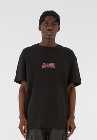 Must mustaga T-särk lühikeste varrukatega, millel on esikeskel punane graafiline tekst. Sile tekstuur, ümar kaelus, mugav lõige.