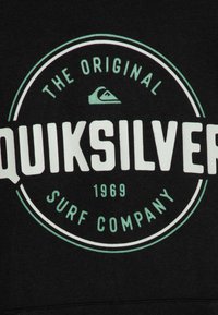 Black sweatshirt featuring a large circular graphic with "Quiksilver" in bold white text, accompanied by light green accents and logo details.