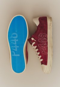Paire de baskets en daim rouge avec des lacets blancs, des semelles beige et des semelles bleues affichant le nom de la marque P448.
