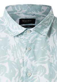 Camicia azzurra chiara con un motivo floreale bianco, dotata di colletto tradizionale e tre bottoni bianchi sulla pattina.