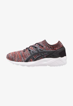 Meerklleurige gebreide sneaker met zwarte synthetische overlays, zwarte veters en dikke witte zool, zijaanzicht op witte achtergrond.