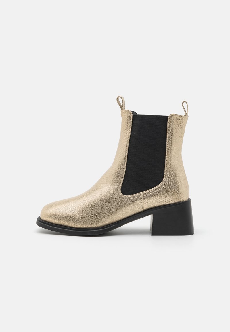 Bottines métalliques dorées à finition texturée, avec des panneaux latéraux élastiques et un talon bloc noir. Dotées d'étiquettes à tirer pour un enfilage facile.