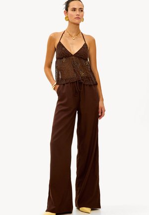 Haut à bretelles marron avec un motif en perles, associé à un pantalon marron ample à corde de serrage et des chaussures jaunes, mettant en avant une texture transparente et une coupe décontractée.