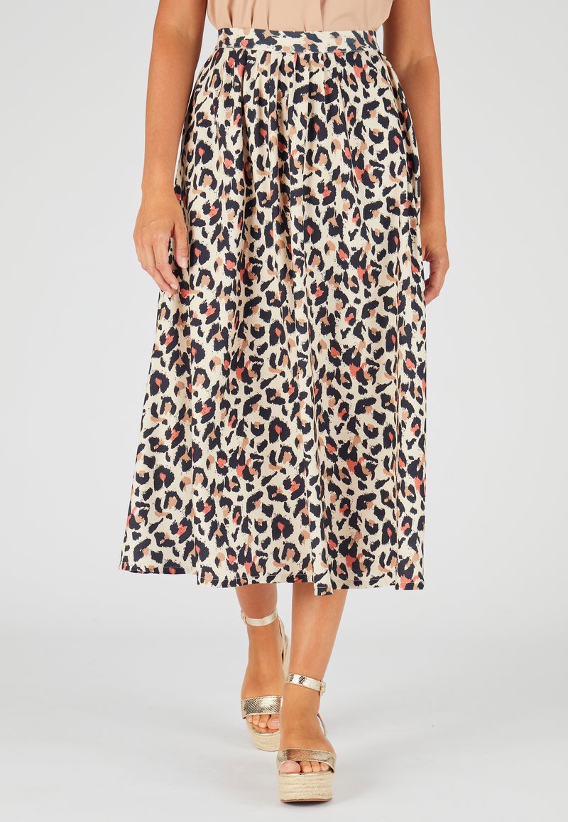 Falda midi acampanada de tela beige con estampado de leopardo negro y rojo. Tiene pliegues y una cinturilla alta. Combinada con sandalias de plataforma doradas.