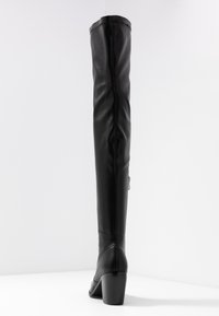 Bottes noires au-dessus du genou avec une finition en cuir lisse, bout pointu et talon épais. Comprend une fermeture éclair sur le côté et des détails cousus.