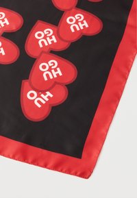 Fekete selyemsál piros szívmintákkal, benne a "Hugo" felirattal; piros szegéllyel befejezve. Simább tapintású felület.