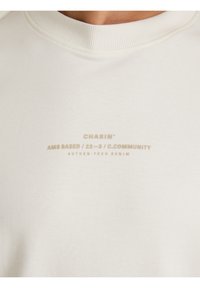 Cremefarbener Sweatshirt aus weicher Baumwolle, mit einem gerippten Rundhalsausschnitt und dezent geprägtem Branding auf der Vorderseite.