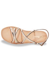 Sandalia plana con correas metálicas doradas, plantilla de cuero natural y diseño minimalista. Presenta una correa ajustable en el tobillo y detalles de costura.