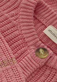Rosa stickad kofta med ett mönster av textur, som har en stor, genomskinlig knapp och en tygetikett med "miny." tryckt på.