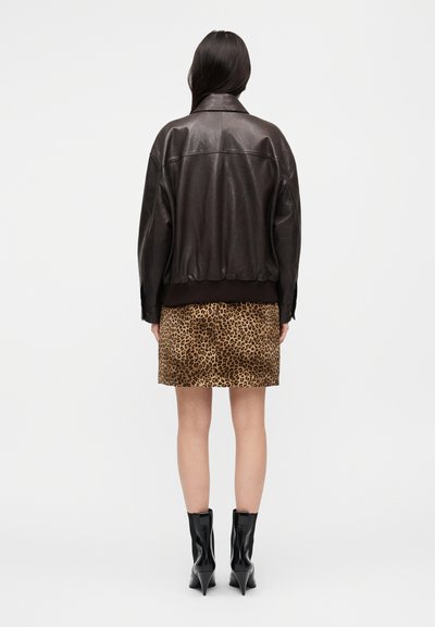 Καφέ δερμάτινο μπουφάν βομβιστή με ριμπ τελείωμα, συνδυασμένο με μίνι φούστα λεοπάρ και μαύρα μυτερά μποτάκια έως τον αστράγαλο.