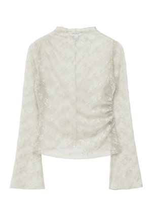 Blusa blanca semitransparente de manga larga con patrón de encaje floral, ligero fruncido en un lado y escote redondo.