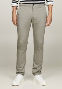 Pantaloni grigi chiari realizzati in tessuto intrecciato, con una vestibilità slim, tasche frontali e chiusura con un solo bottone. Abbinati a sneaker bianche.