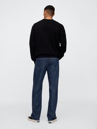 Schwarzer Sweatshirt und dunkelblaue Jeans. Der Sweatshirt hat einen klassischen Schnitt, während die Jeans locker mit geradem Bein sind. Lässige Schuhe sind sichtbar.