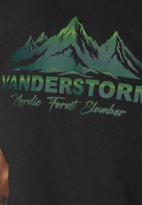 Black fabric t-shirt featuring a green mountain graphic with “VANDERSTORM” in bold letters and “Nordic Forest Slumber” in cursive.