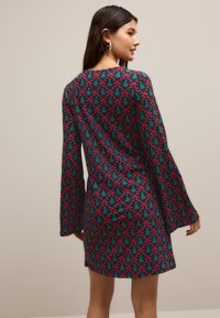 Robe à manches évasées en tissu vert foncé avec un motif floral répétitif rouge et turquoise. Texture lisse, longueur au genou.