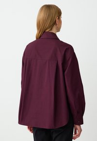 Bordeaux oversized shirt met een klassieke kraag, lange mouwen en met knopen sluitingen. Gemaakt van een gladde stof met een licht gestructureerde afwerking.