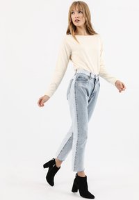 Top a maniche lunghe color crema abbinato a jeans a vita alta di colore azzurro chiaro e stivaletti neri in suede con tacco a blocco. Outfit casual con linee pulite.
