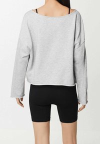Sweatshirt gris surdimensionné avec un large col et des manches longues, assorti à des shorts de cyclisme noirs à côtes. Le tissu semble doux et ajustable.