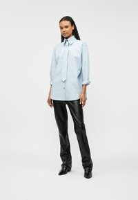 Ανοιχτό μπλε πουκάμισο με μεγάλο μέγεθος και κουμπιά, με αιχμηρό γιακά και γραβάτα, σε συνδυασμό με μαύρα δερμάτινα παντελόνια και παπούτσια με μυτερή μύτη.