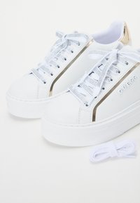 Sneakers bianchi in ecopelle con accenti metallici dorati, lacci glitterati argento e suole spesse in gomma bianca. Inclusa una coppia di lacci bianchi aggiuntivi.