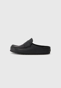 Chaussure noire en cuir à enfiler avec un bout rond, des coutures décoratives et une semelle en caoutchouc texturée. Surface lisse avec des accents minimaux.