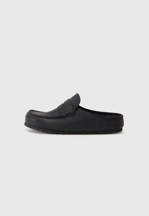 Black leather slip-on shoe with a rounded toe, stitched detailing, and a textured rubber sole. Smooth surface with minimal accents.