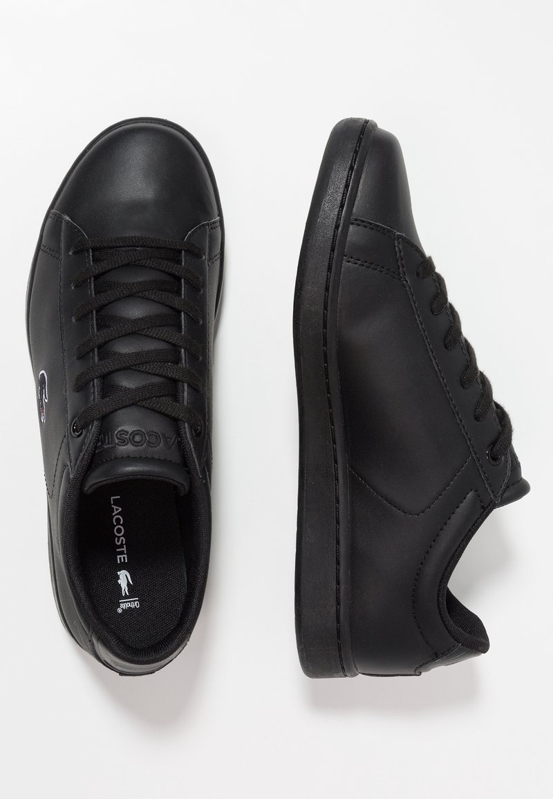 Paire de baskets en cuir noir Lacoste avec lacets noirs, vues de dessus et de côté sur fond blanc.