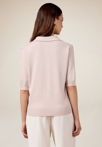 Helles rosa Kurzarm-Pullover mit glatter, strukturierter Oberfläche, ausgestattet mit einem Kragen sowie gerippten Bündchen und Saum, von hinten betrachtet.