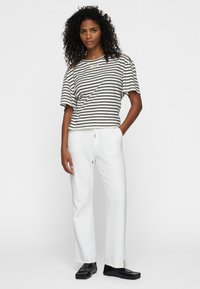 Top a righe a maniche corte in bianco e nero, abbinato a pantaloni lounge bianchi. I pantaloni hanno un cordino e sottili accenti laterali. Scarpe basse nere.