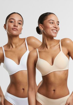 Two bras displayed in white and nude colors with a smooth, soft texture, featuring a plunging neckline and adjustable straps.