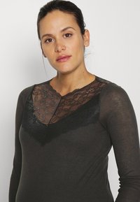 Camisola de mangas longas, cinza escuro, com um decote em V de renda preta e textura canelada. O tecido parece suave, com um corte ajustado.